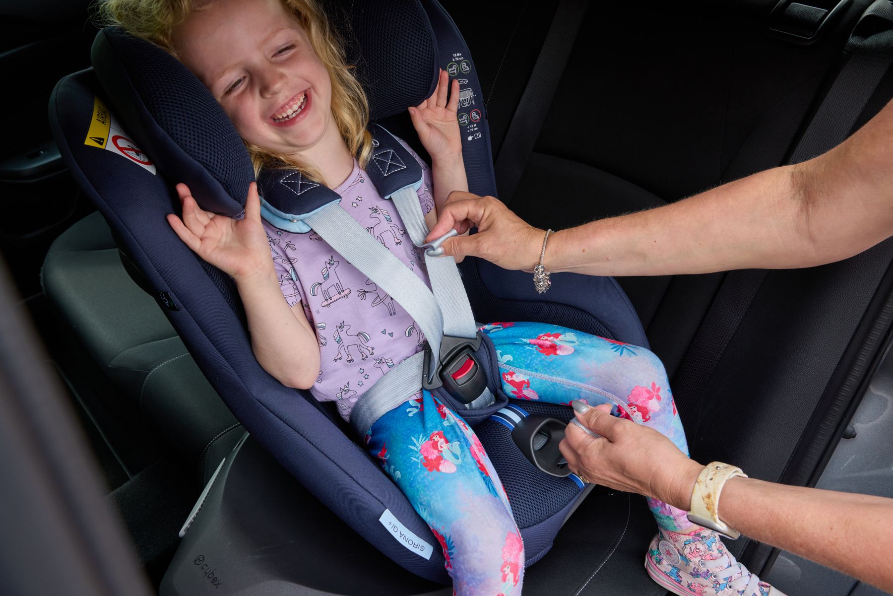A laughing girl being buckled into her car seat