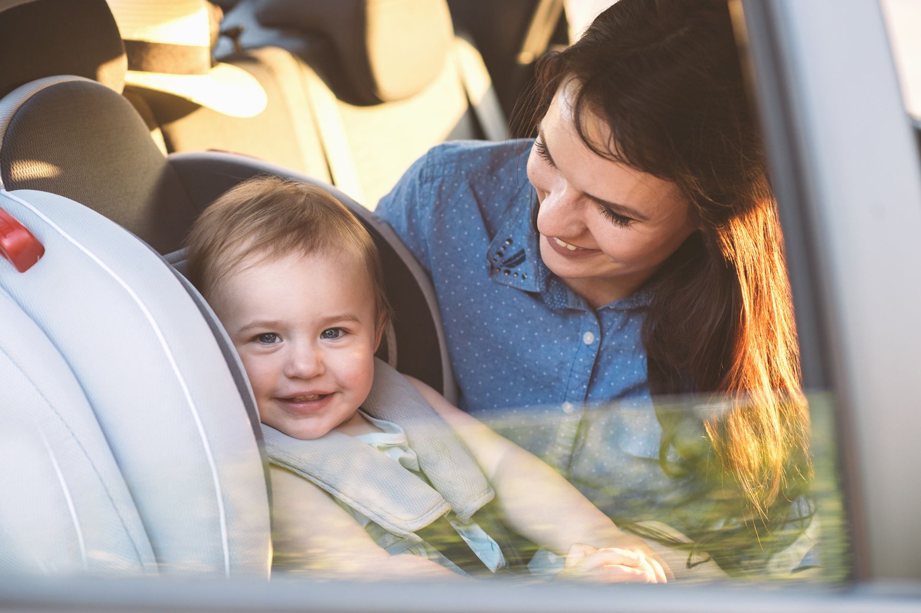A parent smiling at her toddler, safely strapped into a car seat